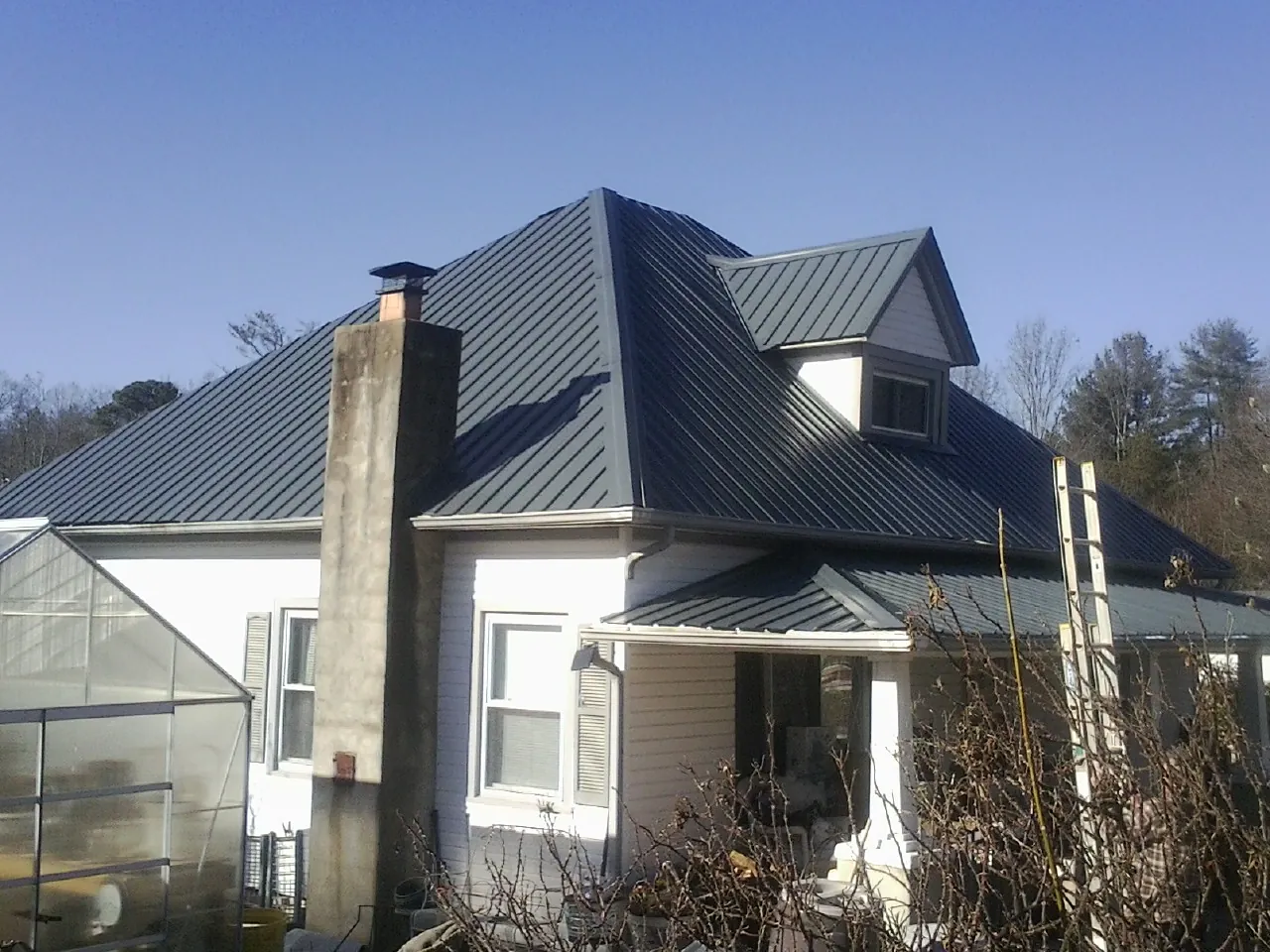 Dark blue standing seam metal roof on a white farmhouse with dormer — Slate & Tile Roof Repair by Roofing Brothers in Savonburg