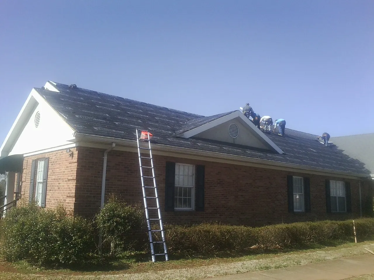 Crew tearing shingles off a brick ranch roof with a ladder set — Emergency Roof Repair work by our crew in Savonburg