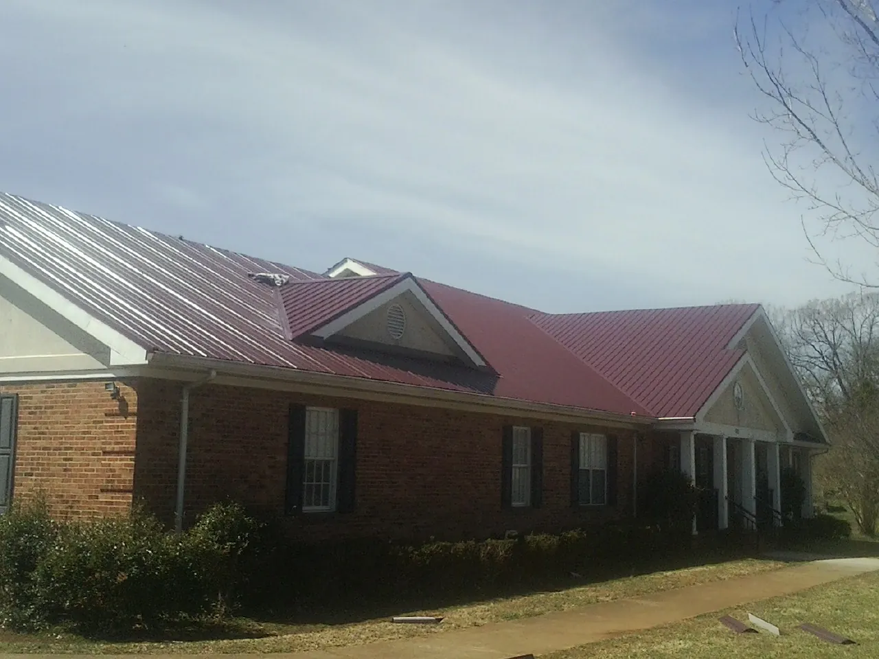 Red metal roof with gabled entries on a long brick building, from a Hail Damage Roof Repair job in Savonburg