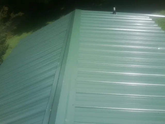 New green metal panels meeting at the ridge of a roof — Flat Roof Repair work by our crew in Savonburg
