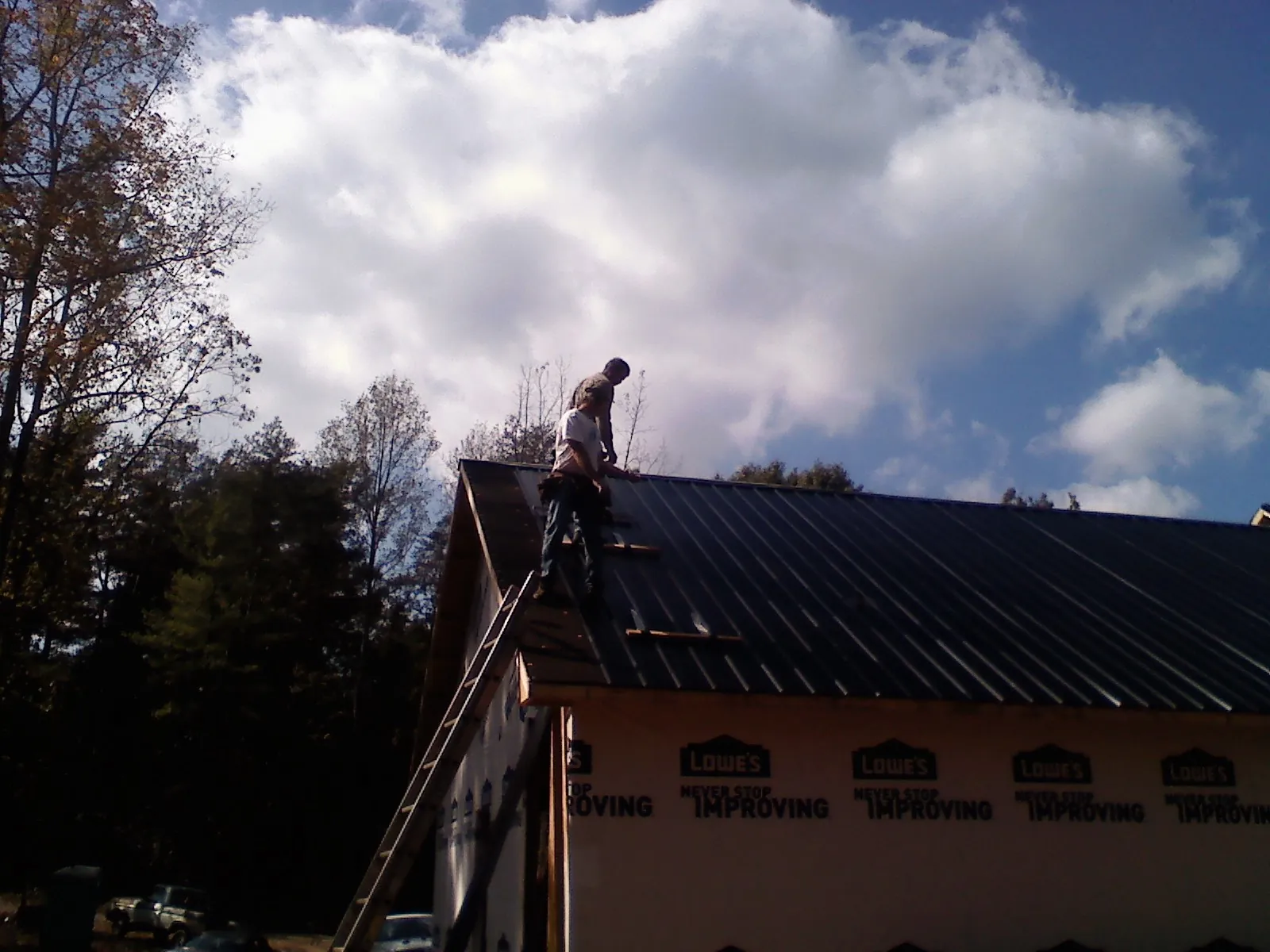 Roofer fastening dark metal panels high against a cloudy sky, from a Roof Inspection job in Savonburg