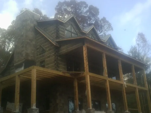 Stone chimney and dormers on a large log home with a timber porch in Savonburg