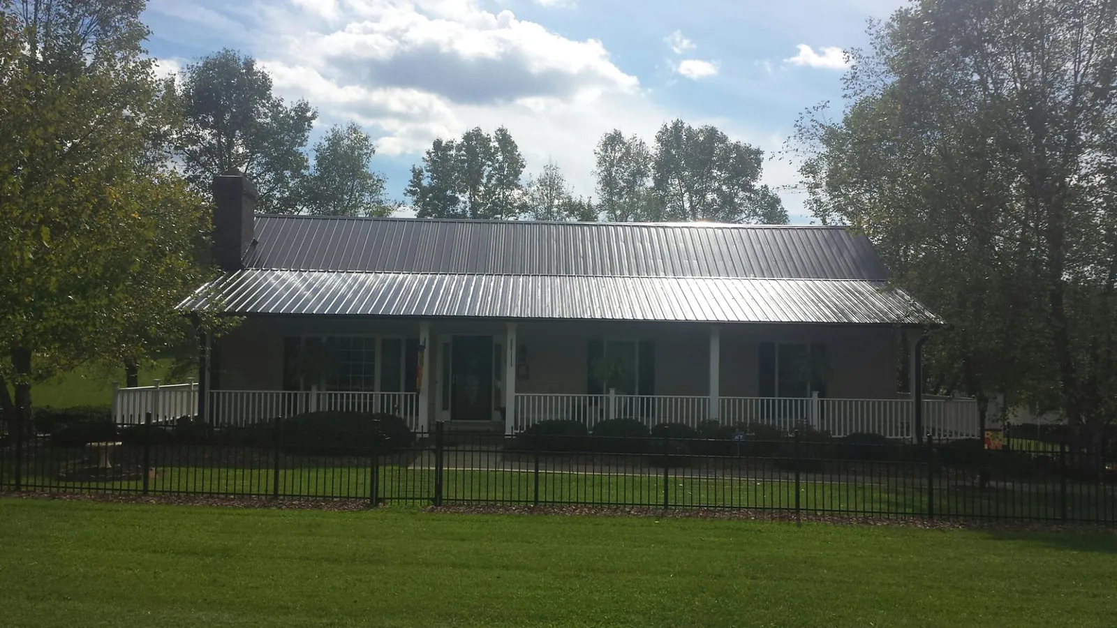 Gray metal roof on a brick ranch with a full width front porch — Gutter Guard Installation work by our crew in Savonburg