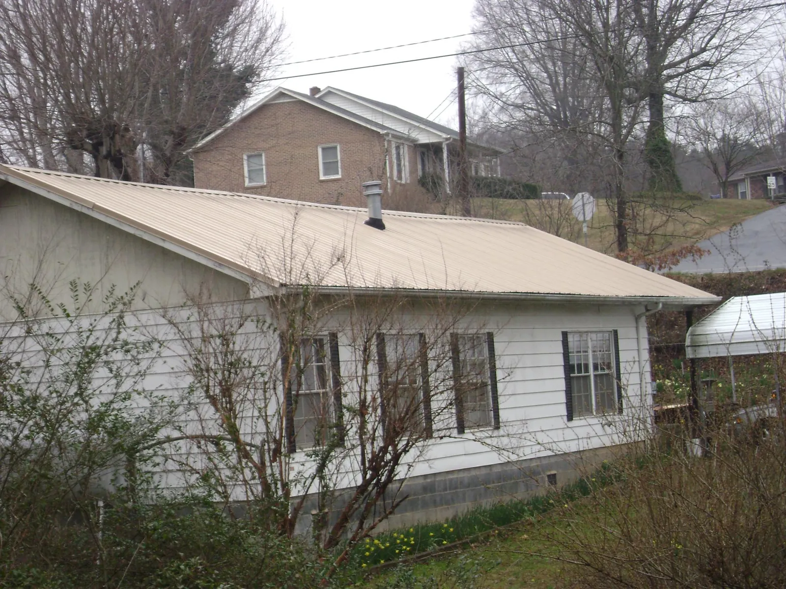 Tan metal roof on a white sided house set into a hillside — Commercial Roofing by Roofing Brothers in Savonburg