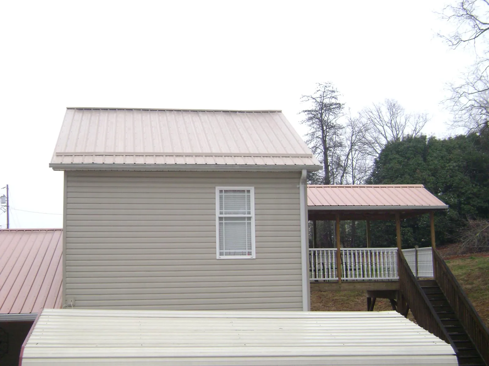 Tan metal roofs on a two story addition and attached porch, from a Roof Replacement job in Savonburg
